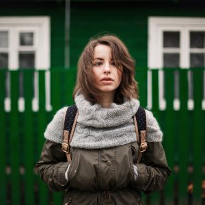 young woman in coat with green fence